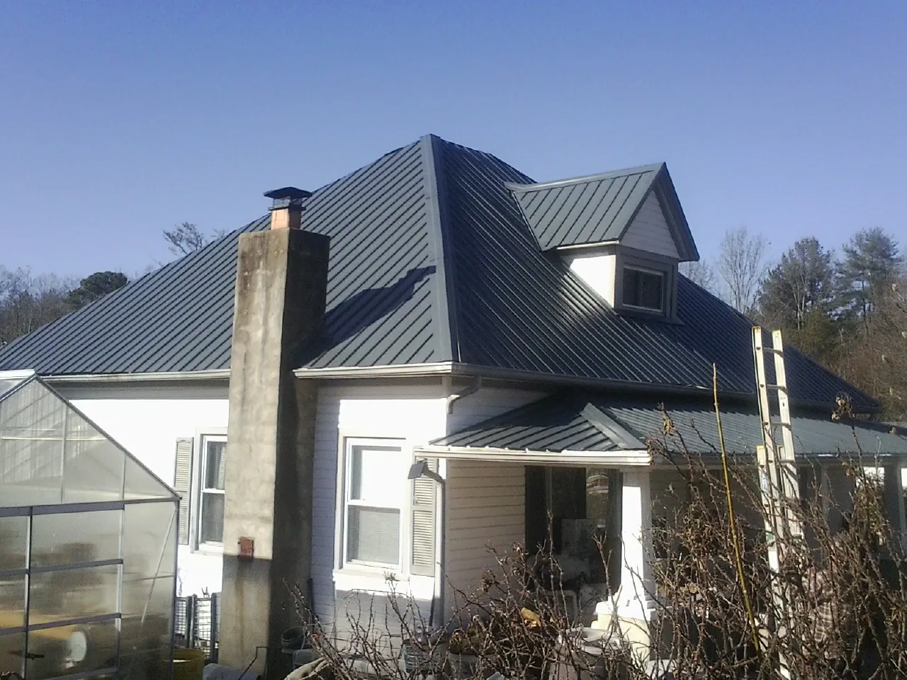 Dark blue standing seam metal roof on a white farmhouse with dormer — Slate & Tile Roof Repair by Roofing Brothers in Margarettsville