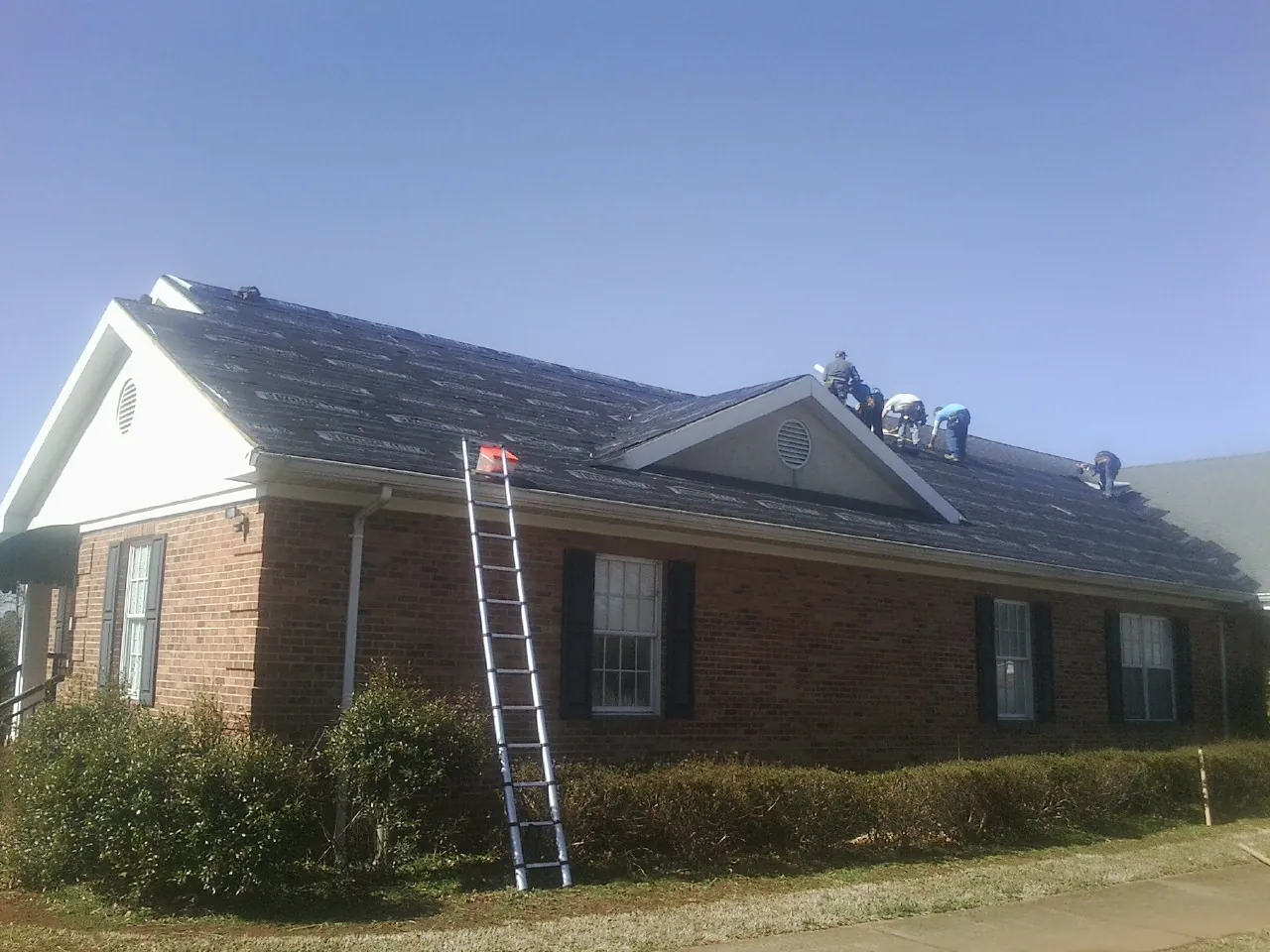 Crew tearing shingles off a brick ranch roof with a ladder set — Metal Roof Repair work by our crew in Margarettsville
