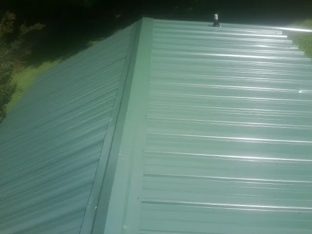 New green metal panels meeting at the ridge of a roof — Flat Roof Repair work by our crew in Margarettsville