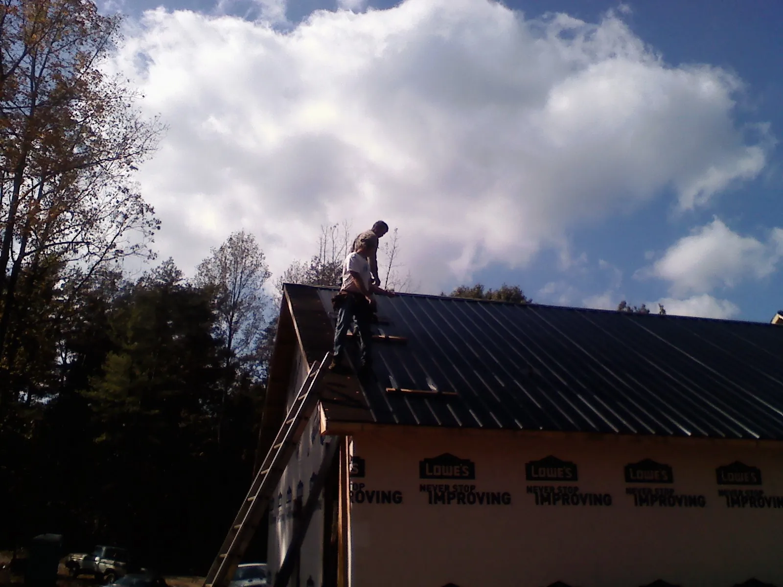 Roofer fastening dark metal panels high against a cloudy sky, from a Roof Inspection job in Margarettsville
