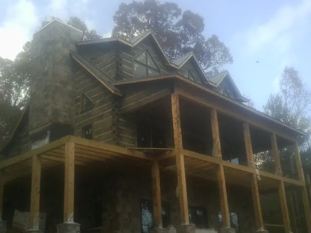 Stone chimney and dormers on a large log home with a timber porch in Margarettsville