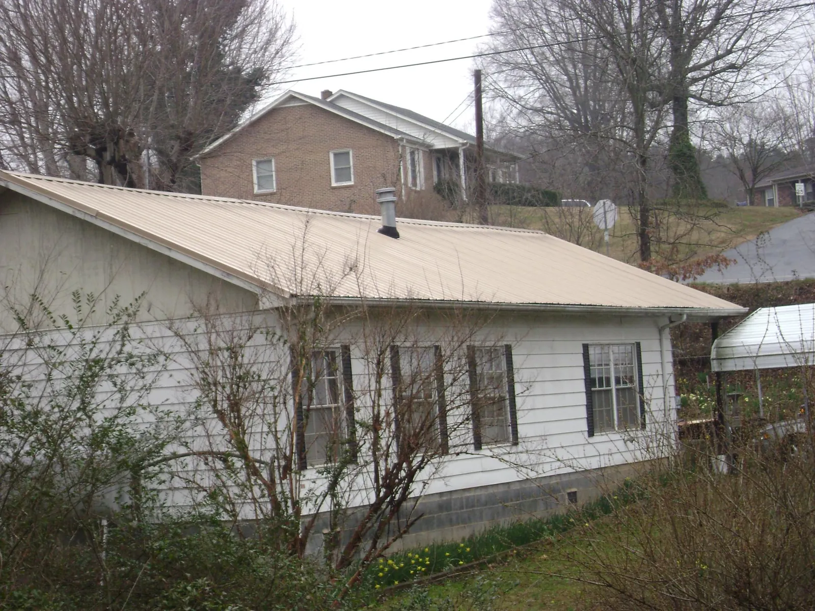 Tan metal roof on a white sided house set into a hillside — Commercial Roofing by Roofing Brothers in Margarettsville