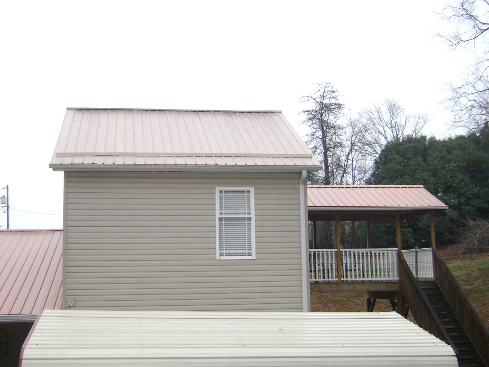 Tan metal roofs on a two story addition and attached porch, from a Roof Replacement job in Margarettsville